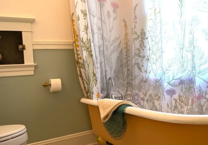 A bathroom with a yellow bathtub, floral shower curtain, toilet, and toilet paper holder.