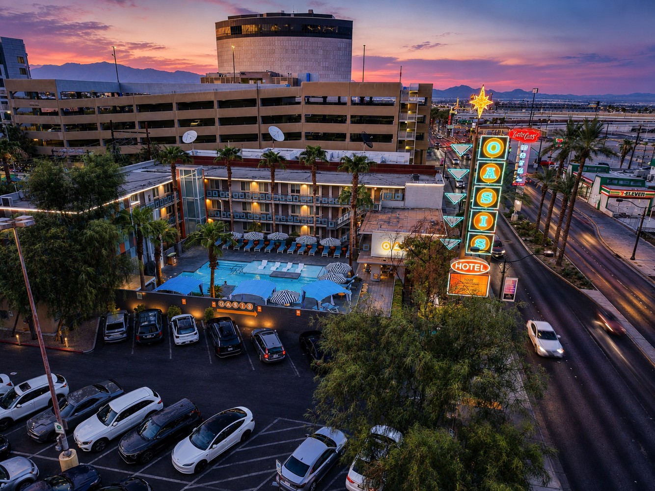 Aerial view of the hotel exterior at sunset, showing the pool, parking lot, and surrounding cityscape.